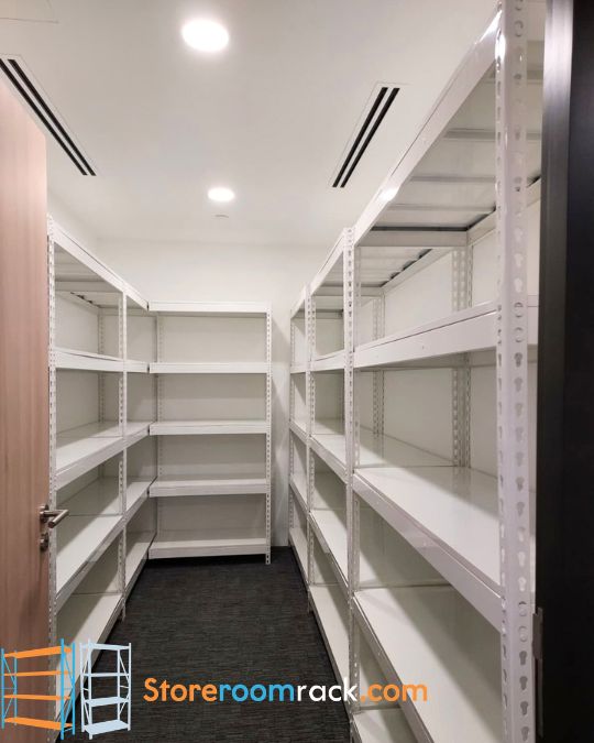 White boltless shelving down both walls of a larger storeroom, one run turning the corner at the far end, with the walkway between them left clear