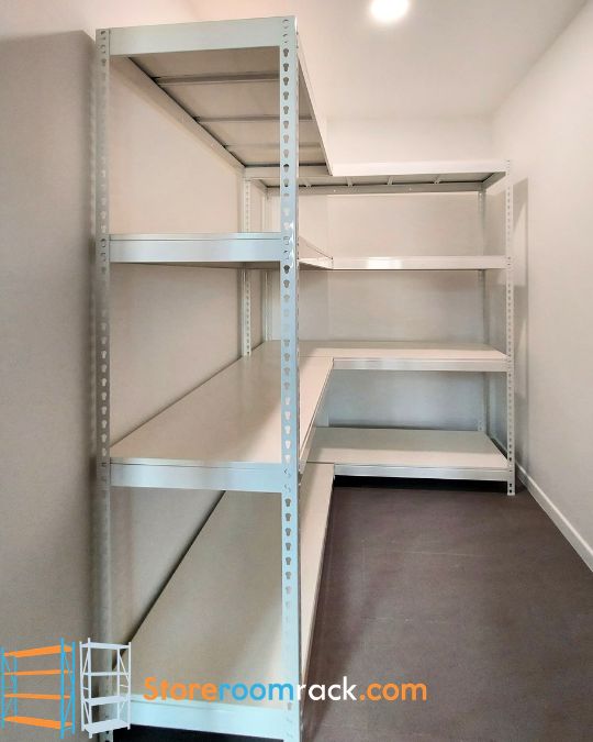 L-shaped rack running down one wall of a narrow storeroom and turning along the end wall, its shelves meeting at the corner with no upright in the way