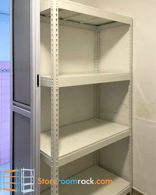 Single straight boltless rack with four white shelf levels standing against the end wall of a household shelter, beside the folding aluminium door